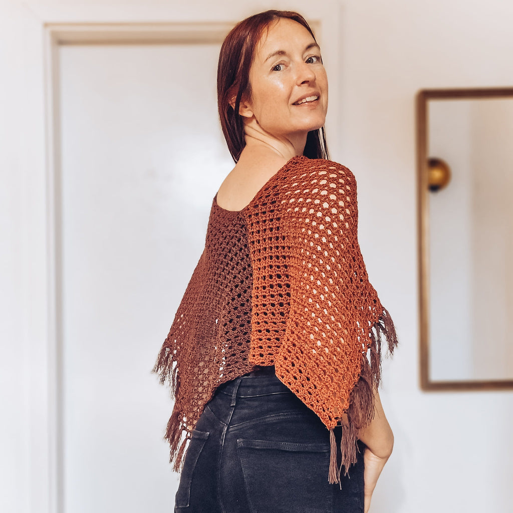 Loops Only Ember Fringe Poncho shawl with fringe detailing, cozy knit fabric, in warm ember color, draped over a model.