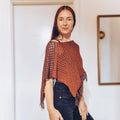 Loops Only Ember Fringe Poncho shawl with fringed edges, cozy knit fabric, in warm ember color, draped on a model.